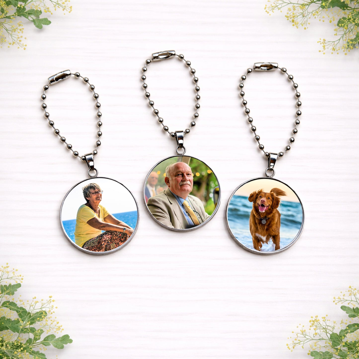 Three personalised wedding bouquet memorial charms with photo portraits displayed on silver ball chains against a soft floral background.