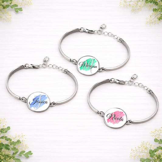 Personalised brushstroke name bracelets with custom names in blue, green and pink designs on silver adjustable bracelets.