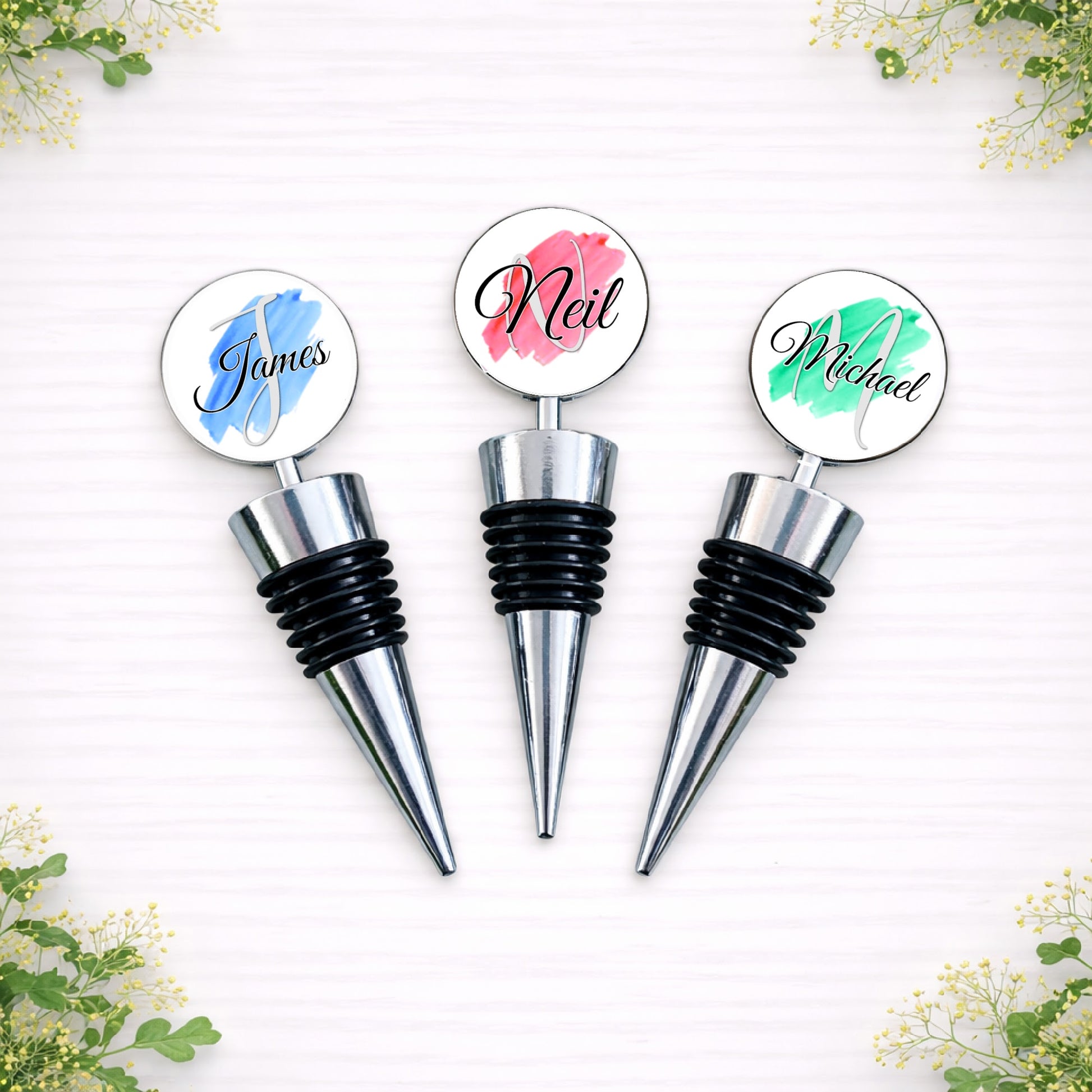 Personalised brushstroke name bottle stoppers for groomsmen featuring custom names in blue, pink and green designs.