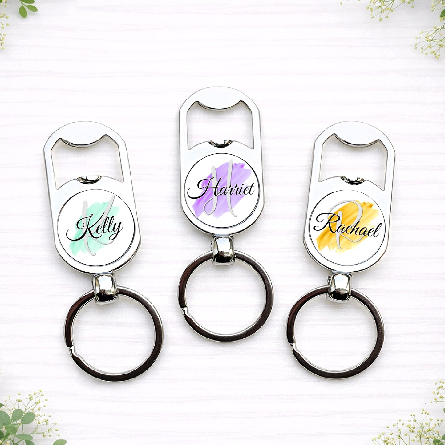Personalised bridesmaid bottle opener keyrings with custom names in pastel brushstroke wedding colours for bridal party gifts.
