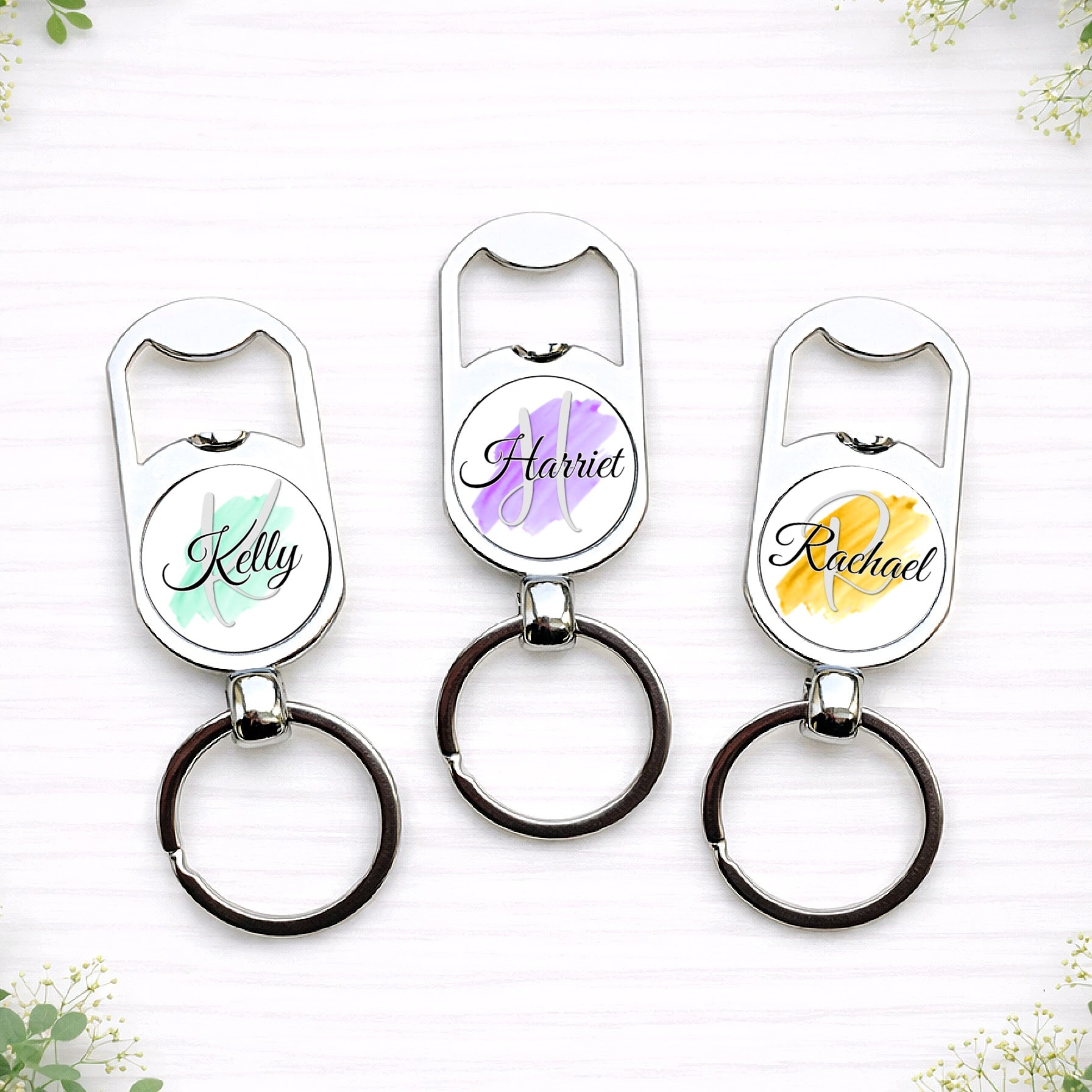 Personalised bridesmaid bottle opener keyrings with custom names in pastel brushstroke wedding colours for bridal party gifts.