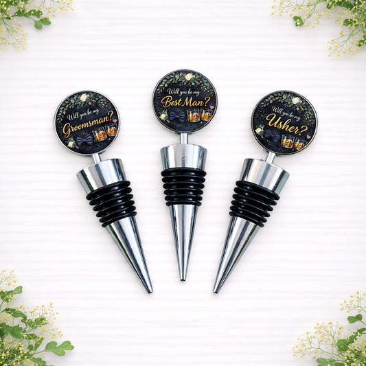 Personalised groomsman proposal bottle stoppers reading “Will you be my Groomsman?”, “Best Man?” and “Usher?” with navy and gold wedding design on silver metal wine stoppers.