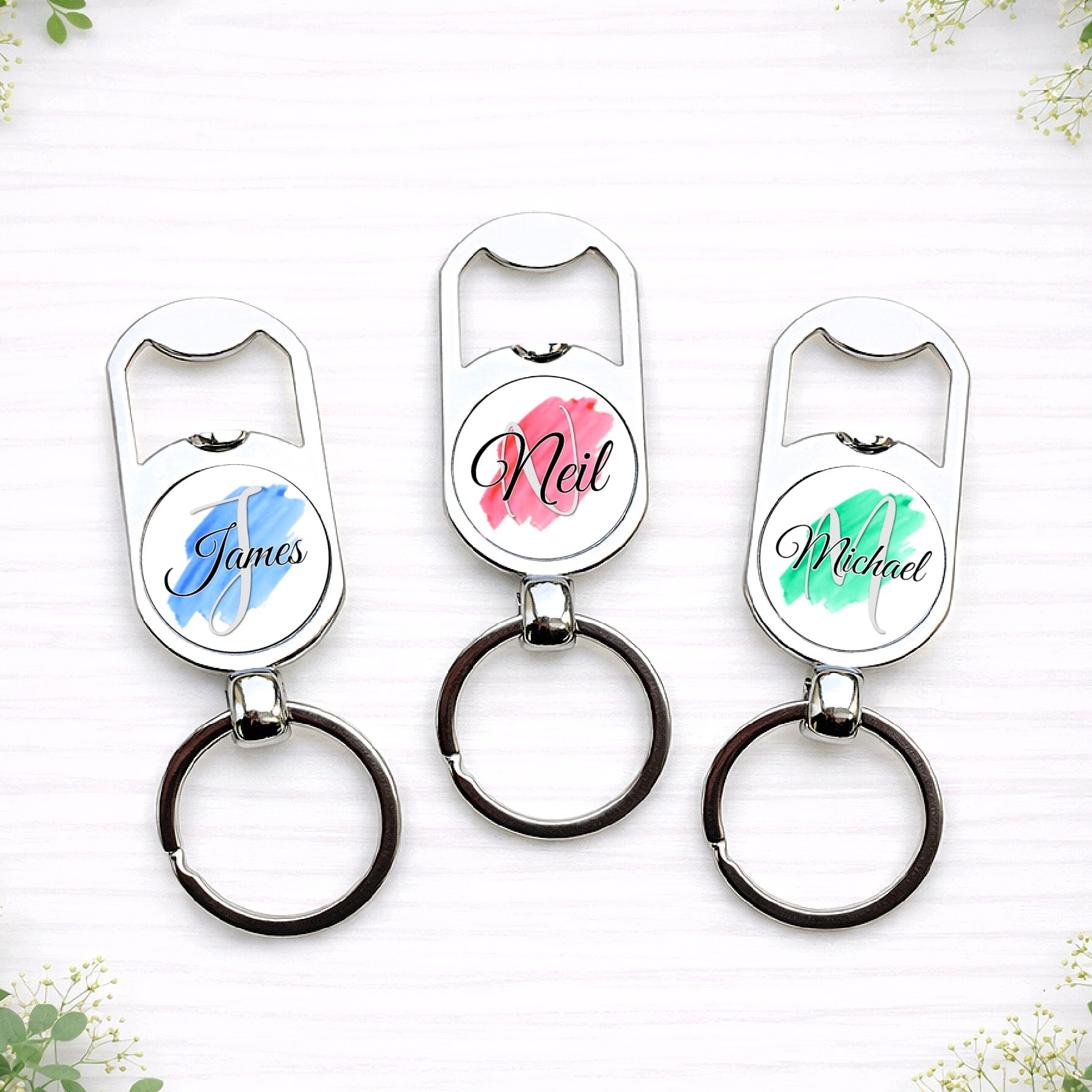 Personalised groomsmen bottle opener keyrings with custom names in blue, red and green brushstroke wedding colours.